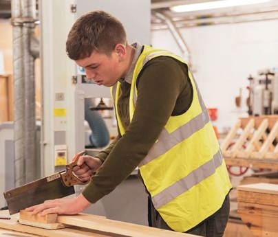 student wearing hi-vis jacket sawing wood in joinery workshop