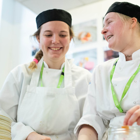 2 female student chefs laughing in training kitchen