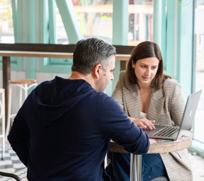 1 man and 1 woman talking looking at laptop on table