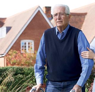 care assistant helps elderly man across garden