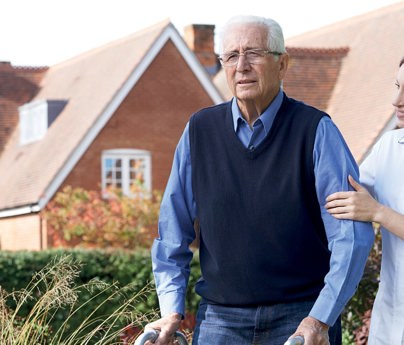 care assistant helps elderly man across garden