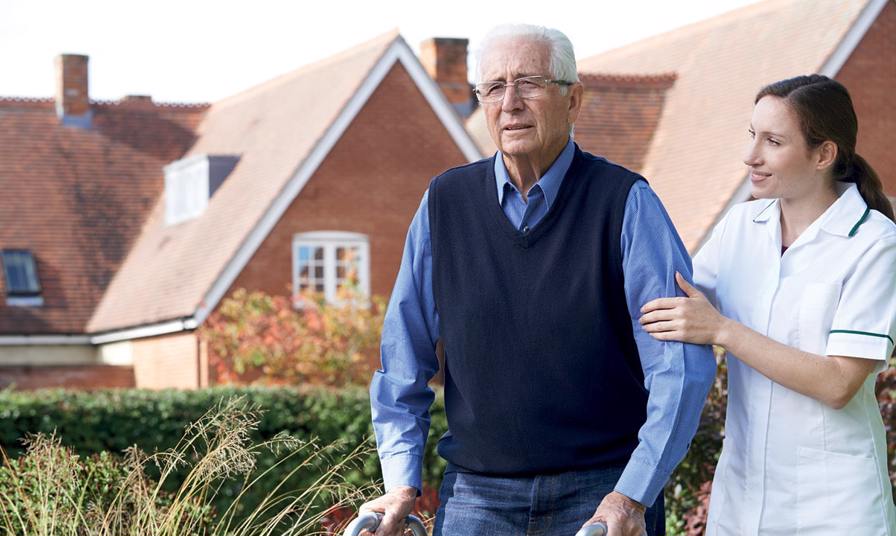 care assistant helps elderly man across garden