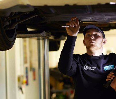 mechanic student stood under car held up whilst he inspects the underside