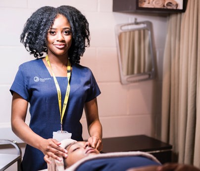 student smiling to cameral with hands on clients temples laying down in beauty salon