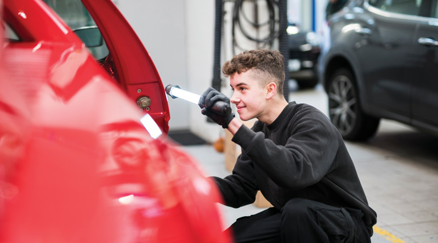 young man checks side of car in mechanics workshop