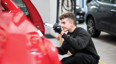 young man checks side of car in mechanics workshop