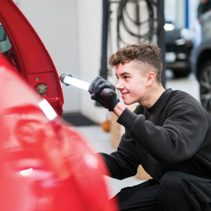 young man checks side of car in mechanics workshop