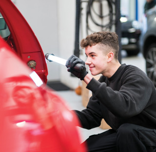 young man checks side of car in mechanics workshop