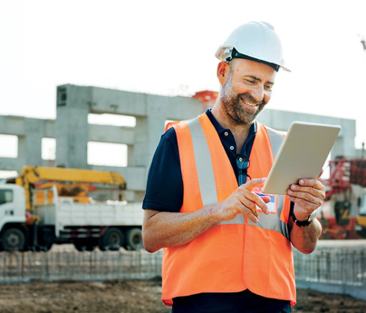 smiling man in high-vis vest and hard-hat in construction site looking at ipad