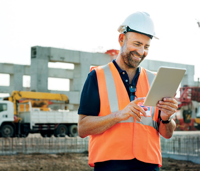 smiling man in high-vis vest and hard-hat in construction site looking at ipad