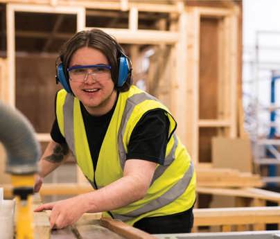 man wearing protective goggles and headphones operates joinery equipment