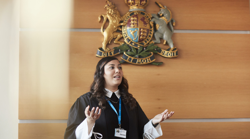 law student stands under crest on wall looking like presenting speech