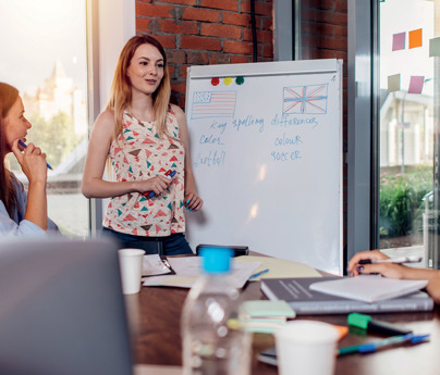 woman stands next to white board with flags of USA and UK with words