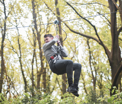 smiling young man zooms down the zip line amongst the trees in the forest