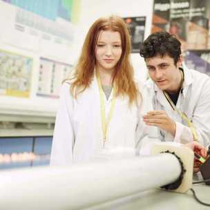 2 science students wearing white lab coats look over an experiment with flames